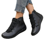 Black faux leather short boots with flat soles, side zippers, and decorative laces, worn with blue jeans.