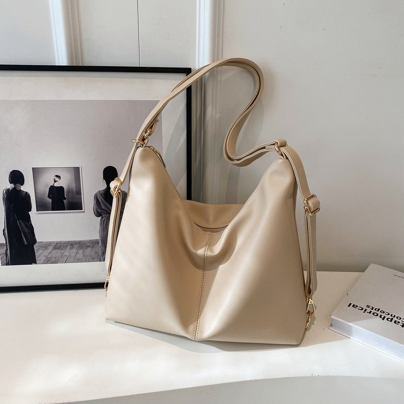 A beige, minimalist PU leather slouchy shoulder bag with gold-tone hardware and adjustable strap on a white surface.