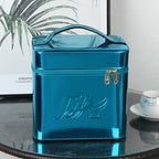 Glossy blue, square portable makeup bag with a top handle, zipper closure, and embossed logo on a glass table.
