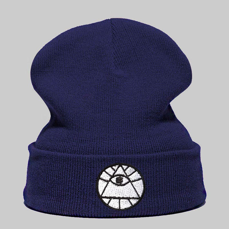 A navy blue knitted winter beanie featuring a white embroidered circular patch of an all-seeing eye pyramid symbol.