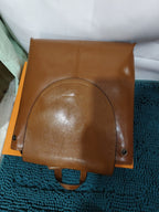 Tan genuine leather retro-style backpack with a curved flap closure and dark metal snap buttons.