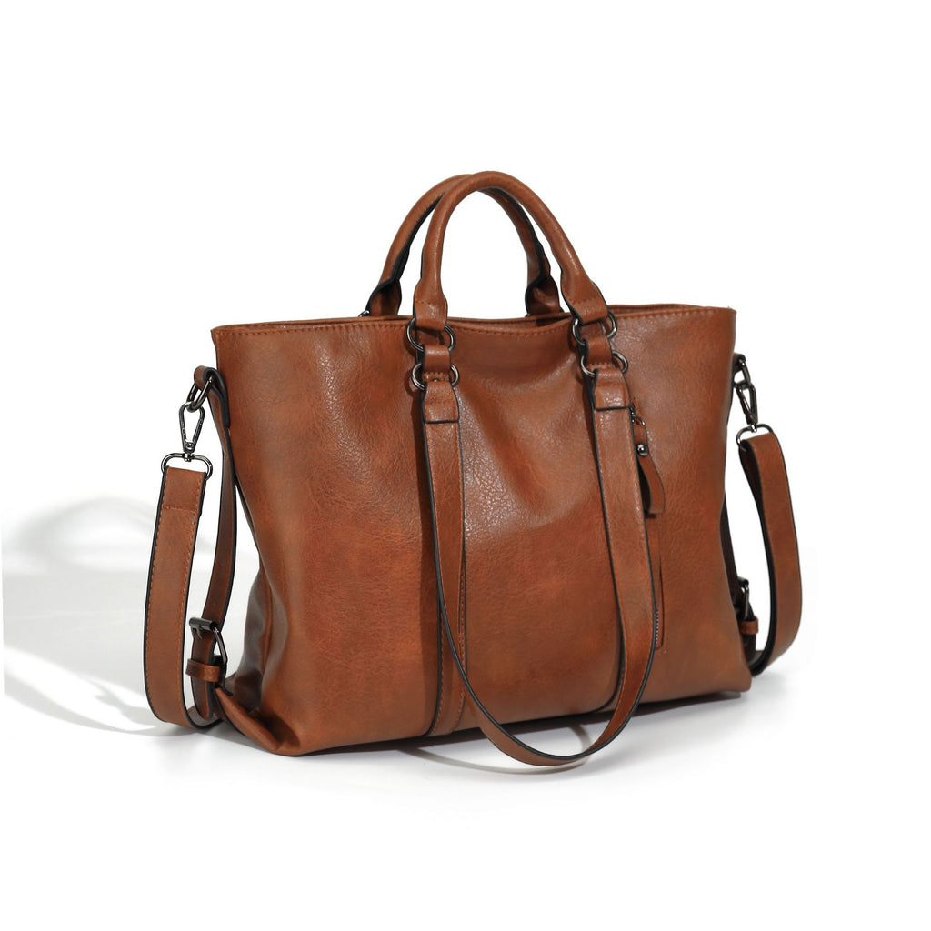 A large, soft brown faux leather tote bag with dual handles, an adjustable shoulder strap, and dark metal hardware.