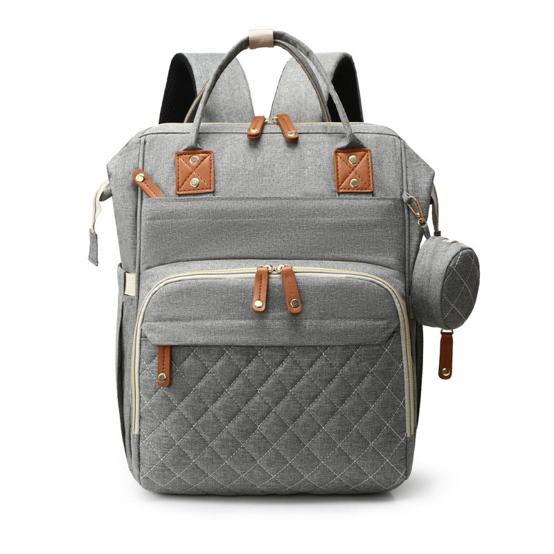 Grey, quilted fabric mummy backpack with tan leather accents, top handles, multiple zippered pockets, and a pouch.