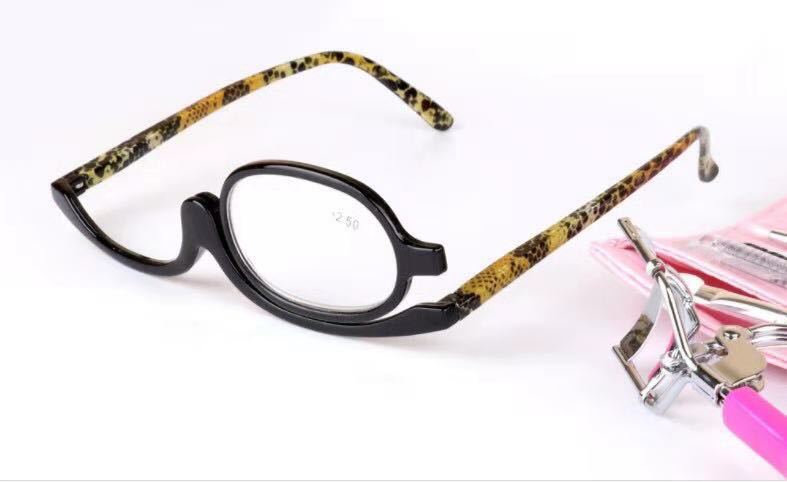 Makeup glasses with a swiveling lens, black frame, and snakeskin-pattern arms, next to a pink lash curler.