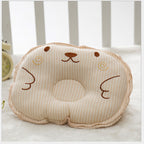 Beige striped baby pillow with a soft, embroidered bear face and a center head-support indentation.