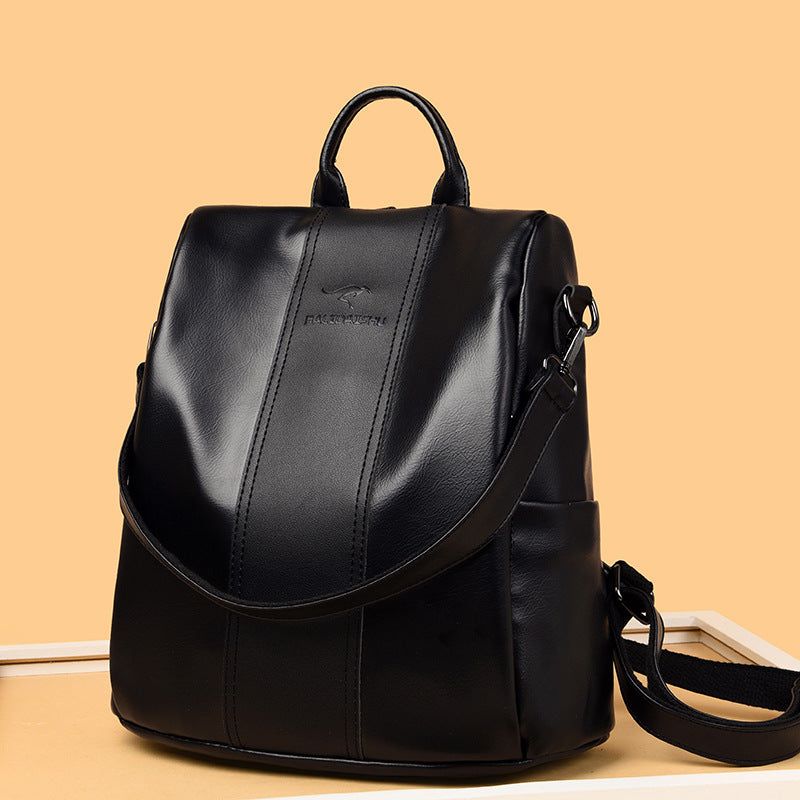 Black soft leather women's backpack with top handle, adjustable straps, and debossed kangaroo logo on a tan background.