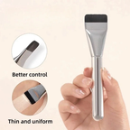 Ultra-thin flat foundation brush with a silver metallic handle and black bristles, held in a hand for makeup application.