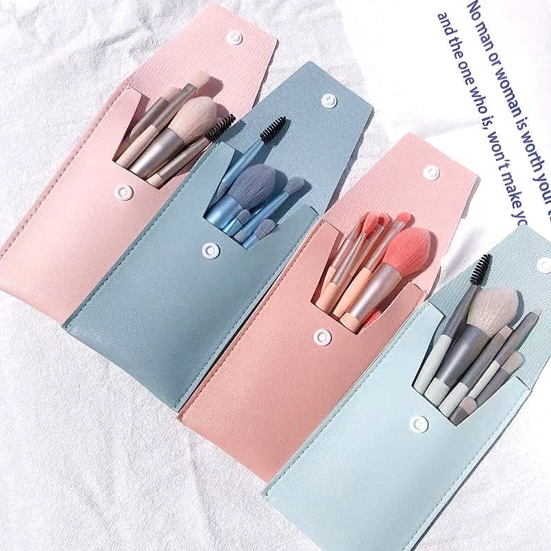 Four portable sets of mini makeup brushes in pastel pink and blue faux leather snap cases on a white fabric background.