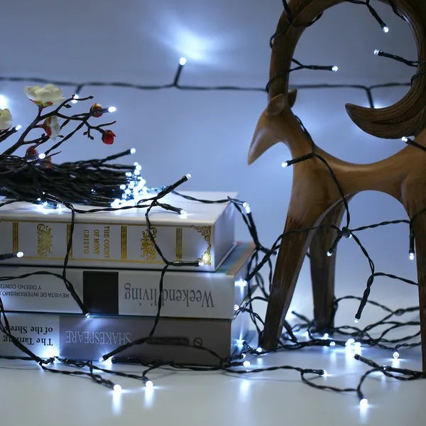 12m solar fairy string lights with bright cool-white LEDs on a black wire, draped around books and a wooden deer decor.