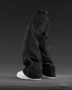Black baggy denim jeans with flame-shaped patchwork, frayed edges, and white sneakers against a dark gray background.