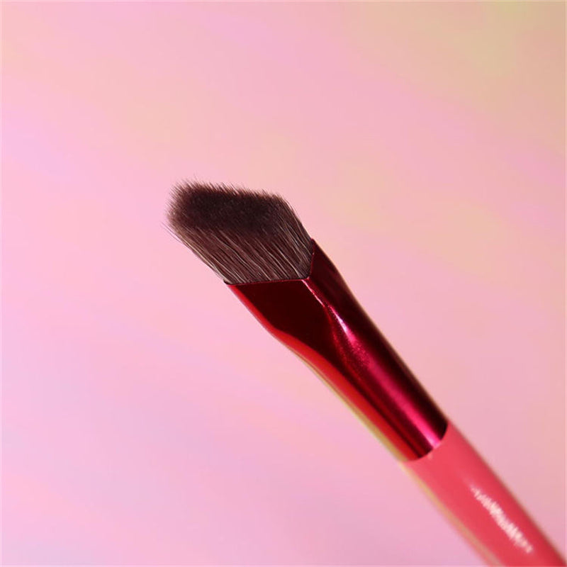 Squared-off angled eyebrow brush with dark brown bristles and a shiny metallic red ferrule against a pink background.