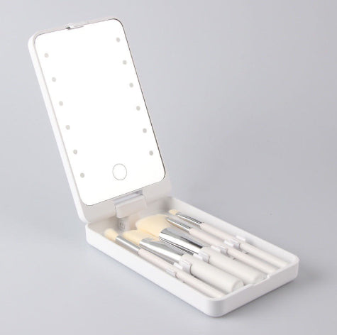 White folding makeup mirror with built-in LED ring lights and a set of matching white makeup brushes inside.