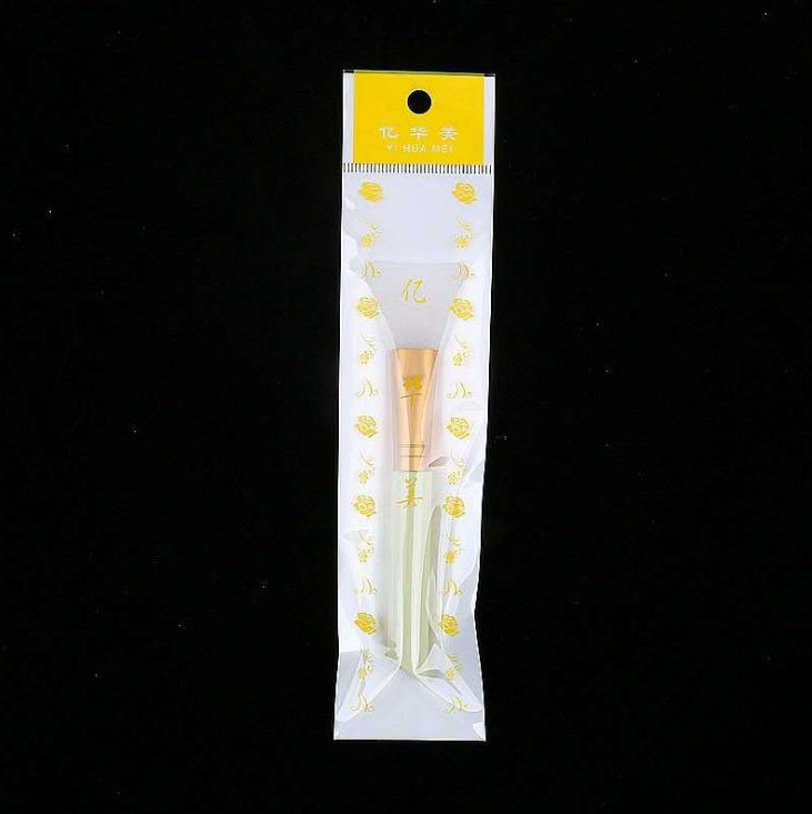 A silicone facial mask brush with a gold ferrule and light handle, packaged in a clear, floral-patterned plastic sleeve.