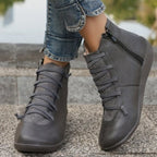 Grey flat ankle boots with side zippers, lace-up fronts, and mixed-texture material worn with cuffed blue jeans.