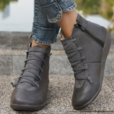 Grey flat ankle boots with side zippers, lace-up fronts, and mixed-texture material worn with cuffed blue jeans.