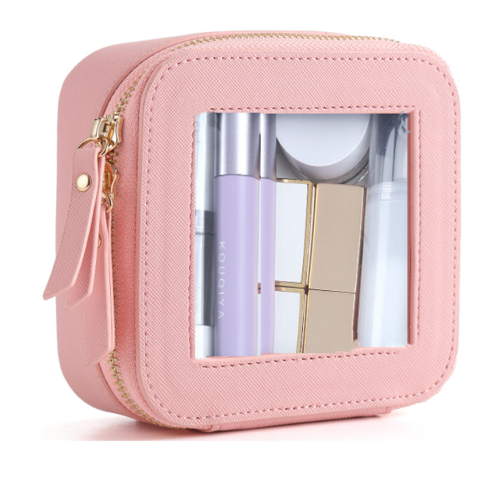 Small, square pink PU leather cosmetic bag with a transparent window, gold zipper, and assorted beauty products inside.