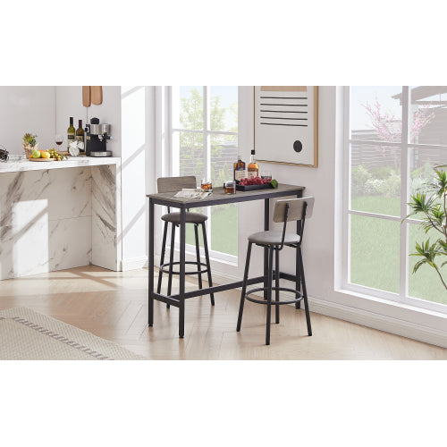 Grey bar table set with two stools featuring padded seats, backrests, and black metal frames in a bright room.