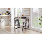 Grey bar table set with two stools featuring padded seats, backrests, and black metal frames in a bright room.