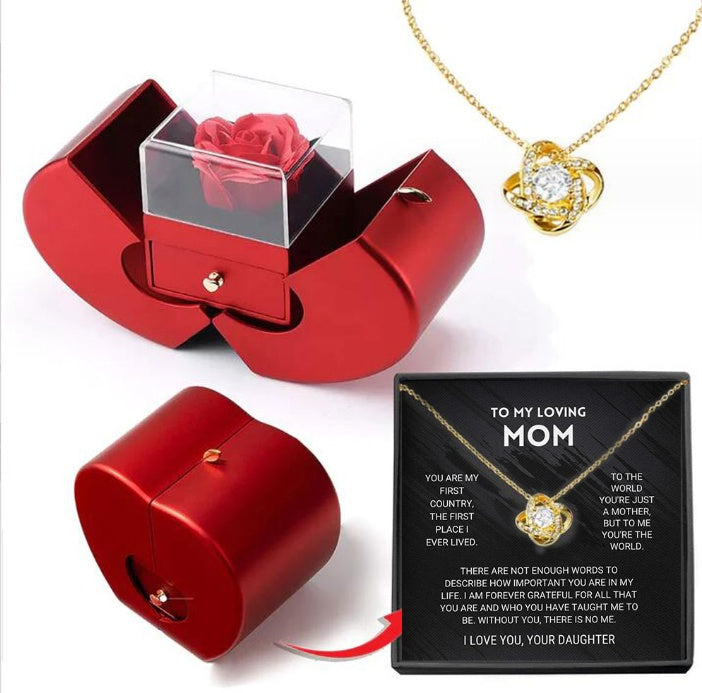 Red apple-shaped gift box containing an artificial red rose, paired with a gold knot pendant necklace and gift card.