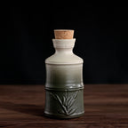 Ceramic sake bottle with a white-to-green gradient finish, bamboo relief detail, and a natural cork stopper.