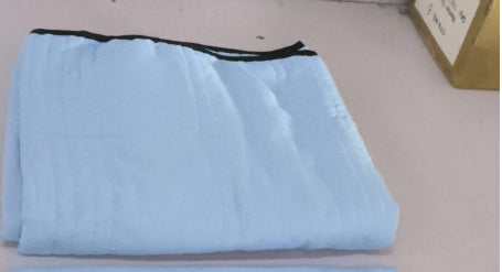 Light blue, folded summer cooling quilt with thin horizontal quilting lines and a black-trimmed edge.