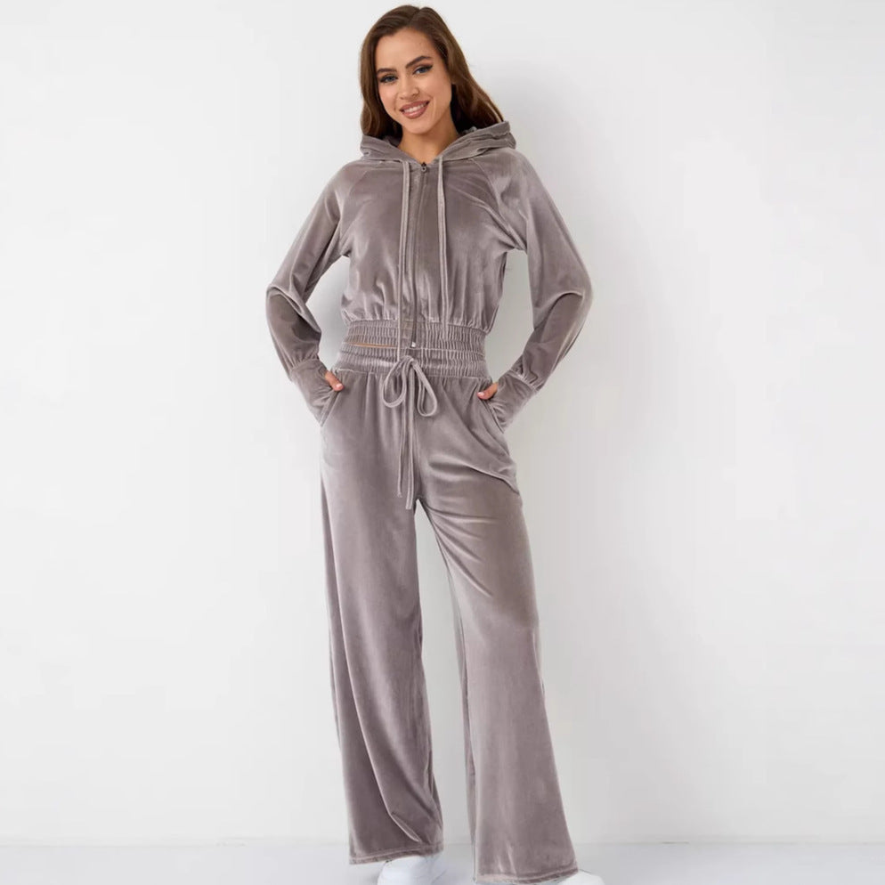 A woman wears a mauve velvet tracksuit with a hooded zip-up jacket and matching wide-leg drawstring trousers.