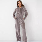 A woman wears a mauve velvet tracksuit with a hooded zip-up jacket and matching wide-leg drawstring trousers.