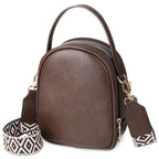 Small coffee-brown crossbody purse with a top handle, dual zippers, and a patterned adjustable strap on a white background.