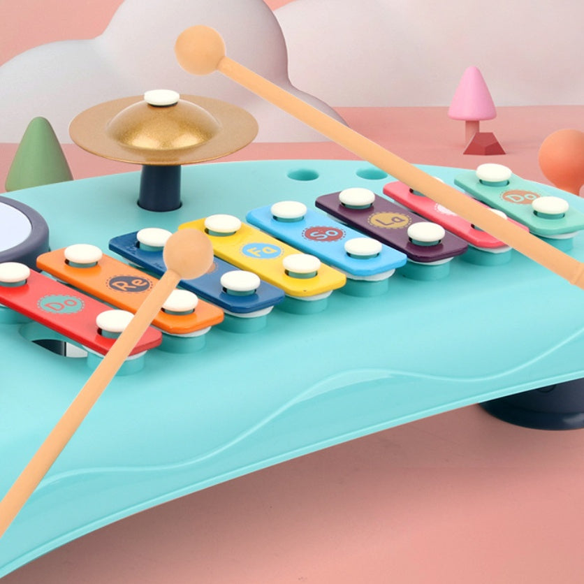 Blue plastic xylophone toy with colorful metal bars, a gold cymbal, and two wooden mallets on a pink background.