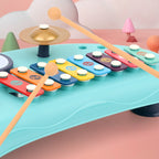 Blue plastic xylophone toy with colorful metal bars, a gold cymbal, and two wooden mallets on a pink background.