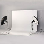 Studio backdrop stand set with white background, black and silver lighting umbrellas, and metal tripod stands.