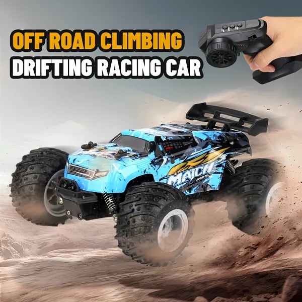 Blue and black off-road RC monster truck with large treaded tires and remote controller on a dusty dirt track.