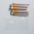 Set of 12 makeup brushes with champagne handles, gold ferrules, and soft synthetic bristles in a plastic bag.