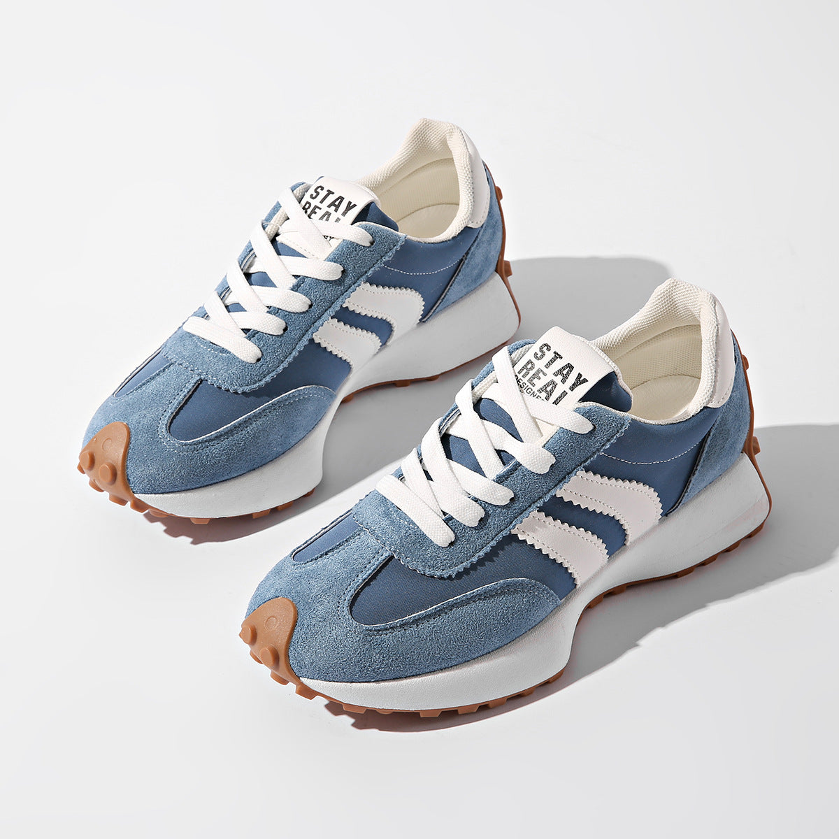 Blue and white lace-up sneakers with suede overlays, chunky white soles, gum tread, and "STAY REAL" tongue labels.