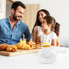 White electric mug warmer with a cup of tea on a table, shown next to a smiling family having breakfast.