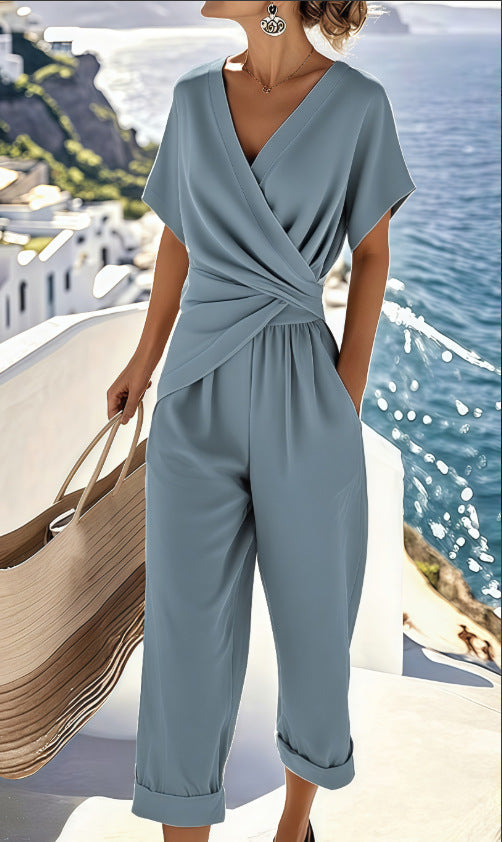 A woman wears a slate-blue two-piece set with a draped V-neck top and matching cuffed cropped trousers.
