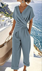 A woman wears a slate-blue two-piece set with a draped V-neck top and matching cuffed cropped trousers.