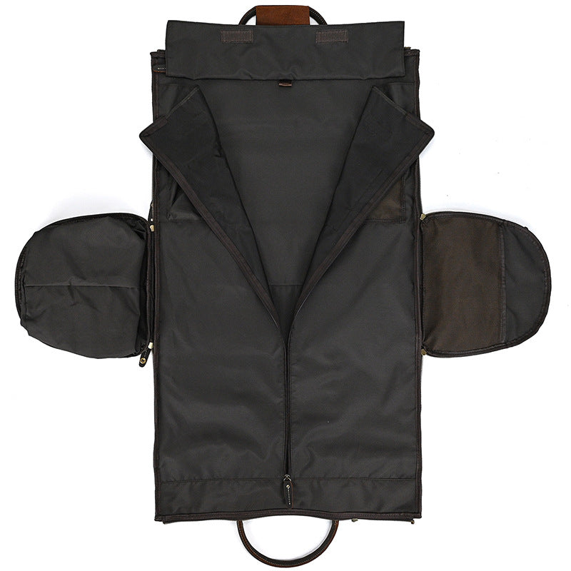 Unfolded black fabric garment bag with leather accents, featuring zippered side compartments and a central zipper.