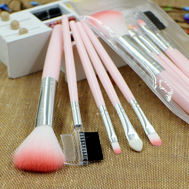 Five pink makeup brushes with silver ferrules and soft, dual-toned bristles on a textured brown background.