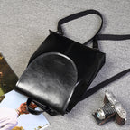 Black genuine leather women's messenger-style backpack with a flap top and adjustable fabric straps.
