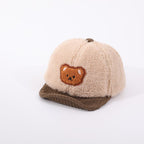 Beige fuzzy baby cap with brown corduroy brim and a cute embroidered bear patch on the front.