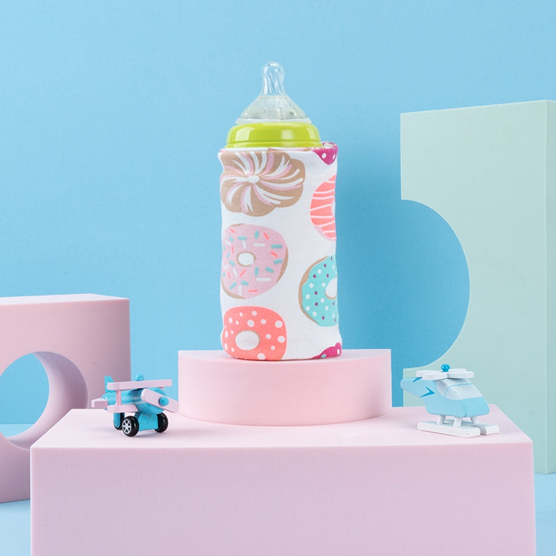 A donut-patterned fabric USB baby bottle warmer sleeve standing on a pink pedestal against a light blue background.