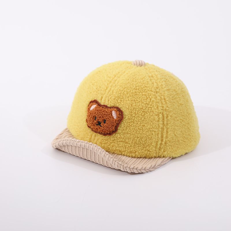 Yellow fuzzy baby hat featuring an embroidered brown bear face and a tan corduroy brim, against a white background.