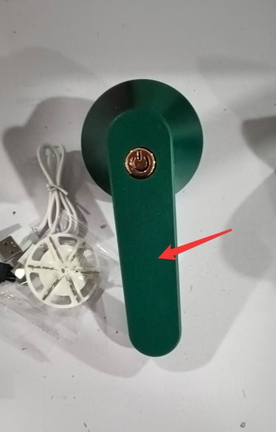 Green handheld lint remover with a gold power button, charging cable, and replacement blade, seen from above.