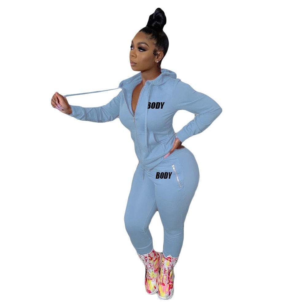 A woman wearing a light blue, zip-up hooded tracksuit with "BODY" printed on the chest and hip pocket.