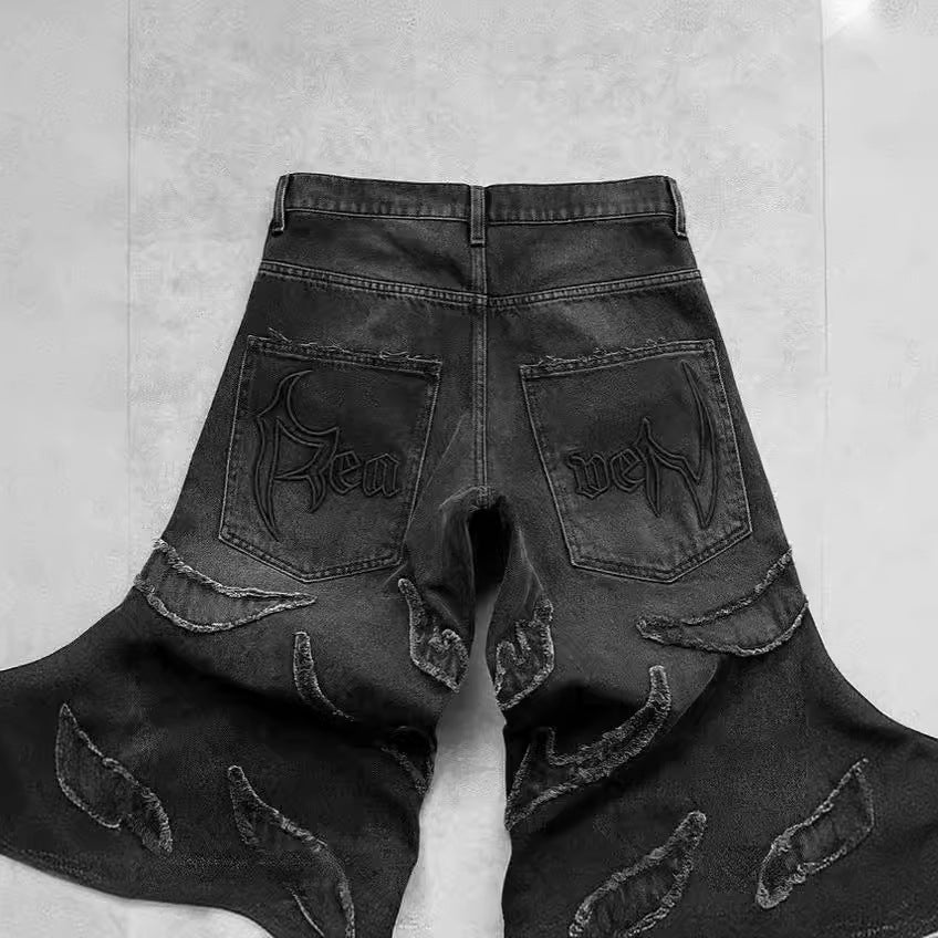 Black baggy denim jeans with frayed patchwork detailing and embroidered gothic script on the back pockets.