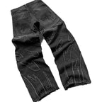 Black baggy denim jeans with frayed flame-shaped patches and gothic-style embroidery on the back pockets.