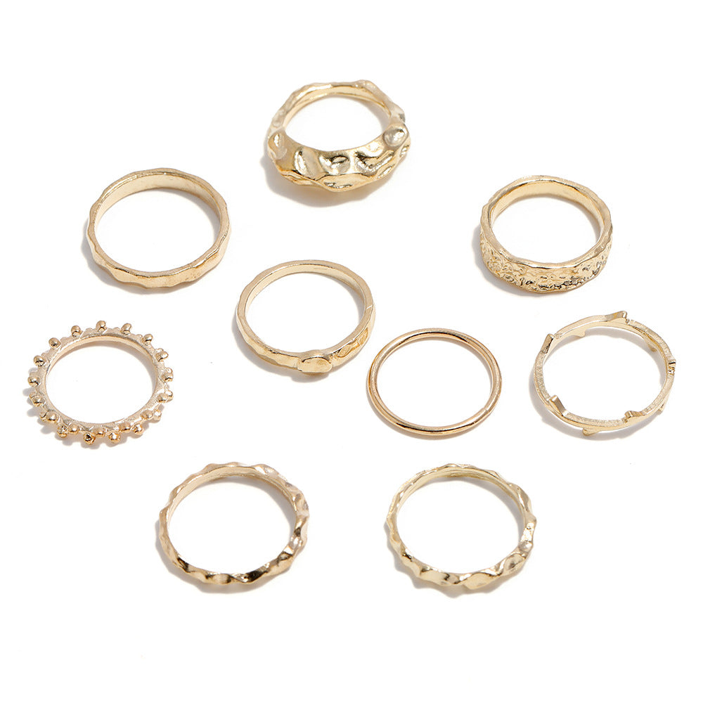 A set of nine gold-toned metal rings featuring various textures, including smooth, hammered, and beaded designs.