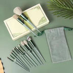 13-piece sage green makeup brush set with soft, light-colored bristles, a storage box, and a fabric drawstring bag.