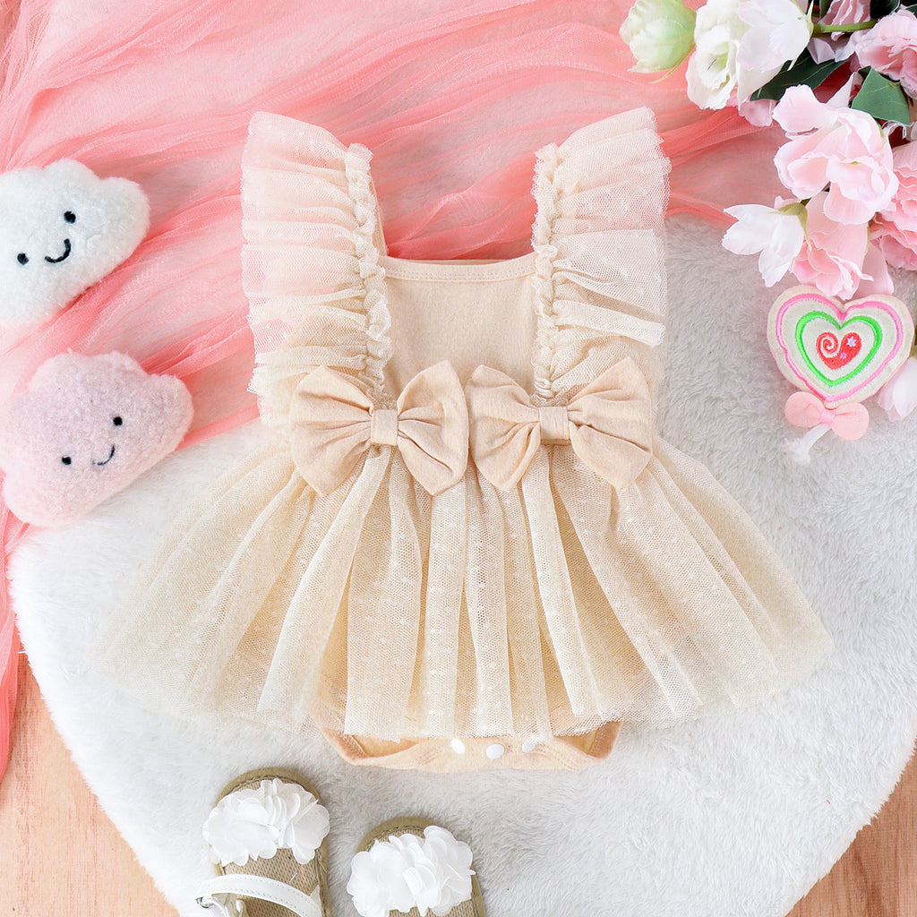 Beige baby jumpsuit with a ruffled tulle skirt, two front bows, and soft fabric, displayed with flowers and decor.